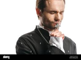 young, serious catholic priest kissing holy cross with closed eyes isolated 