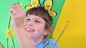 Video: A little girl hid behind yellow daffodils against a green  background. Happy child with bee caps is