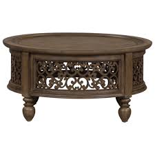 Two round iron and wood coffee tables sit on a gray and tan patterned rug in front of cane and rattan accent chairs placed facing a light gray couch topped with white and black pillows and positioned beside a round end table topped with. Liberty Furniture Parisian Marketplace Relaxed Vintage Round Cocktail Table With Open Design Standard Furniture Cocktail Coffee Tables