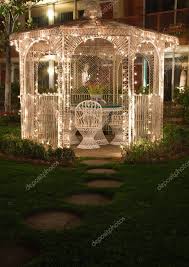 A White Wicker Gazebo With Chairs And A Table Is Lit Up At Night By Several Small White Lights Gazebo Lighting Garden Gazebo Gazebo