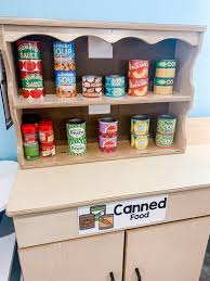A wide shot of a pantry full with grocery items and white baskets. Grocery Store Dramatic Play Center For Preschoolers