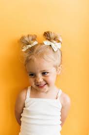 Yellow Background Kids Braided Hairstyles With Beads Two Floral Bows Blonde Hair In Two Messy Buns Baby Girl Hairstyles Baby Girl Hair Baby Hairstyles