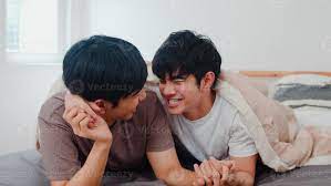 Handsome Asian gay couple talking on bed at home. Young Asian LGBTQ guy  happy relax rest together spend romantic time after wake up in bedroom at  modern house in the morning concept.