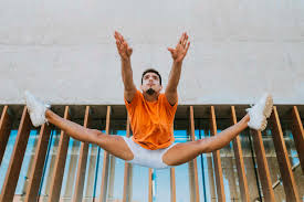 Junger Mann mit gespreizten Beinen, der gegen eine gebaute Struktur  springt, lizenzfreies Stockfoto