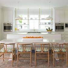 Gorgeous kitchen features a pair of crystal chandeliers over center island with tons of storage space topped with gray quartz countertop framing two sinks with hook and spout faucets fitted with u shaped dining banquette. Kitchen Island Banquette Design Ideas