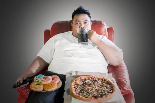 Homem obeso detém rosquinhas enquanto assiste tv — Foto © realinemedia  #102534440