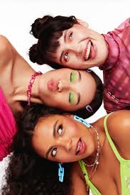 Three females styled in brightly-colored wardrobe and makeup with heads  stacked making silly faces