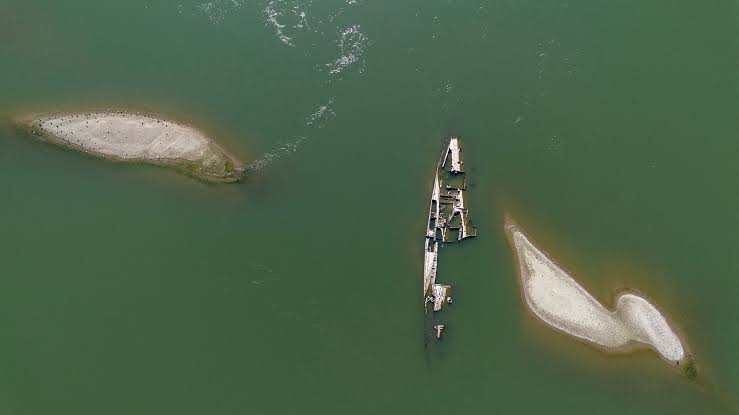 A rusted World War II German warship hull protruding from the muddy banks of the receding Danube River.