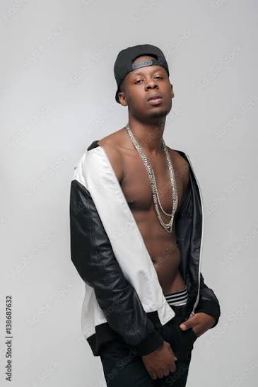 Photo Stock Young african american gangster guy. Problem of substance abuse, crime, social issues, drugs. Ghetto, challenge to society, cheeky, cool, rebellious. Grey background with free space | Adobe Stock