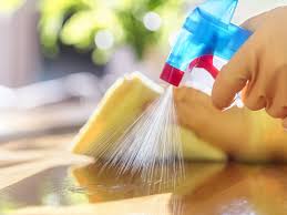 Professional cleaning in action: a gloved hand spraying cleaner on a coffee table with another hand ready to wipe with a cloth, emphasizing house cleaning services.