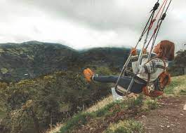 The swing hangs from two ropes tied to a tree branch next to a rickety tree house on the top of a cliff. Swing At The End Of The World In Ecuador Adventure Catcher