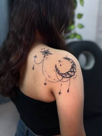 🌙 This is an ornamental moon tattoo with flowing lines and a small geometric pattern. It's placed to complement the natural shape of her shoulder, designed to stay discreet yet expressive at
