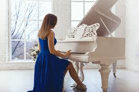 Mulher em um vestido de noite azul tocando em um piano branco ...