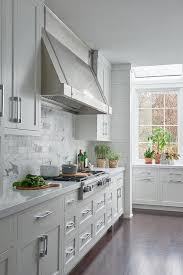 White Shaker Kitchen Cabinets Fitted With Polished Nickel Pulls Flank A Stainless Steel Range Hood Mounted Trendy Kitchen Tile Modern Kitchen Kitchen Examples