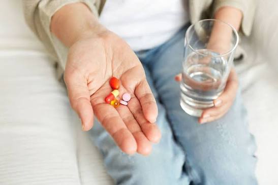 A person holding several pills in one hand next to a glass of water, about to take multiple medications at once