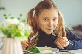 Cute blonde teen girl eating eggs benedict with knife and fo
