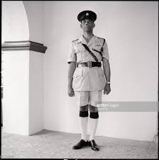 Vous avez une question ? A Jamaican Police Officer Stands Guard Wearing An Official Uniform Police Officer Police Officer Uniform How To Wear