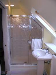 White cabinetry, trim, and ceiling paint carry light through the space, but a darker gray accent wall helps accentuate the interesting ceiling. Sloped Shower Wall Small Bath Sloped Ceiling Bathroom Attic Bathroom Small Bathroom