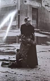 A powerful photo showing a priest holding a dying soldier while bullets are  fired around them, Venezuela, 1962. Priesthood is Love Priesthood is  Sacrifice Priesthood is Compassion Priesthood is Humanity Be Human,