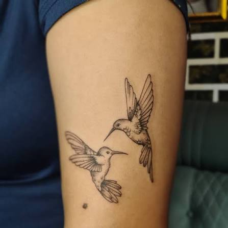 The tattoo depicts two hummingbirds in flight, typically symbolizing: 1. Freedom & Joy – hummingbirds represent lightness and the ability to enjoy life's moments. 2. Energy & Resilience – their rapid wingbeats