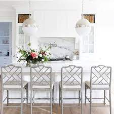 Modern white kitchen with knobless cabinets and a peninsula with wood surface attached to a white table island with mirror legs and a pair of stylish cube stools on. Real Life Thoughts Kitchen Bar Stools Home Decor Stools For Kitchen Island