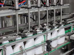 컨베이어 위를 지나가는 병에 8개의 노즐이 동시에 하강하여 액체를 주입하는 자동 충진기 전경