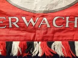 This reproduction, exacting in every detail, features the blood red silk background with white lettering and a black swastika on a white circle and trimmed with alternating red, black & white fringe. Deutschland Erwache Standard Flag