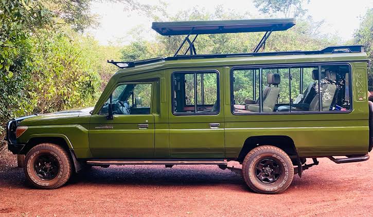 A green 4x4 safari Toyota Land Cruiser driving on a dirt road toward the volcanic mountains in Rwanda