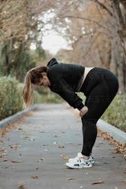 Tired plus sized woman relaxing by bending over on footpath stock photo