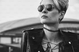 Ritratto di giovane donna tatuata audace con i capelli corti in occhiali  rotondi all'aperto, guardando lontano. Concetto di donna forte, sicura di  sé e audace foto