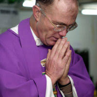 U.S. Marine Corps CPL. David Washington (left), and PVT. Daniel Angelone  (right), both assigned to India Company, 3rd Battalion 3rd Marine Regiment,  listen as Chaplain Paul Evers reads from the Bible during