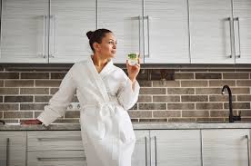 Premium Photo A Beautiful Woman In A White Waffle Robe Is Leaning On The Kitchen Countertop And Looking Away Drinking Lemon Water As A Healthy Morning Habits