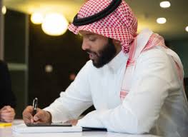 صورة مقربة رجل اعمال سعودي خليجي على المكتب باجتماع مع فريق العمل يسجل ملاحظات بالقلم شركة سعودية باللباس السعودي التقليدي بيئة عمل صورة 3284 مكتبة الصور
