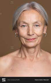 Portrait of naked senior woman with grey hair in front of brown background  stock photo - OFFSET
