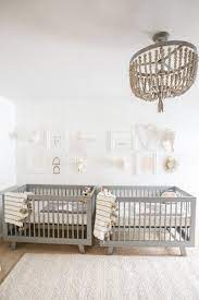 A gender neutral nursery with retro wooden furniture, a navy chair, a boho rug and shelves. Bebe Com Estilo Twin Babies Nursery Nursery Twins Twin Nursery Gender Neutral