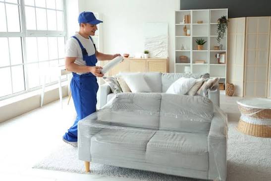 Professional movers wrapping sofa and furniture with moving blankets and protective film