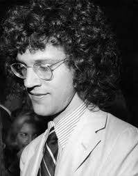 Plano medio de John Rubinstein (medio perfil izquierdo) con gafas, mirando  hacia el suelo