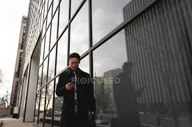 71,790 modern building front premium high res photos. Front View Of Young Well Dressed Asian Businessman Using Mobile Phone While Walking Past Modern Building On Street In The City Cellphone On The Go Stock Photo 250242694