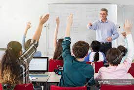 Download teacher classroom stock photos. Male Teacher Calling On Students In Classroom Sitting Gesturing Stock Photo 202436464