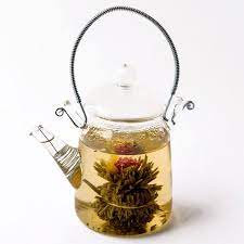 Teapot and glass cup with blooming tea flower inside against wooden background. Flowering Glass Teapot Our Flowering Glass Teapot Is A Beautifully