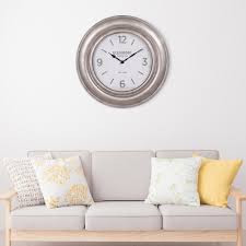 The clock features a black case, with a white face and black roman numerals. Pinnacle Glenmont Wide Silver Wall Clock Ractae Home Decor