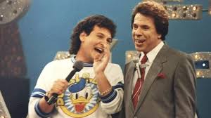 Gugu Liberato e Faustão em programa de TV dos anos 80, sorrindo e segurando microfones. Gugu usa camiseta do Pato Donald.