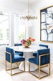 A Round White Dining Table Finished With Gold And Blue Sapphire Dining Chairs Under A Brass And L Dining Room Inspiration Modern Dining Room White Dining Table