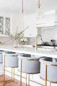 A contrasting kitchen island allows you to introduce new color and texture to the room in an understated yet impactful way. Well Appointed White And Gold Kitchen Boasts Gray Linen Barrel Back Counter Stools Place White Modern Kitchen Modern Kitchen Design Kitchen Design Modern White