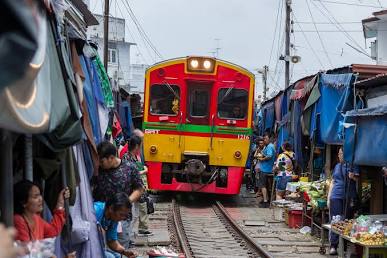 Market stalls retract within inches of the train as it crawls into Mae Klong Station., AI generated