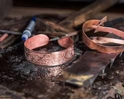 A Cambodian artisan hammering a copper bracelet in a workshop.