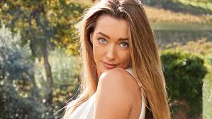 Penny Lane smiles over shoulder in white top amid lush greenery for SI Swimsuit.