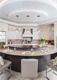 White kitchen with a large and long center island with a marble countertop. Kitchen Island Trends Luxury Kitchen Design Curved Kitchen Custom Kitchen Island