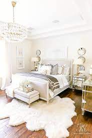 Glam bedroom with gray blue walls paint color, mirrored console table nightstands with gold trim, ivory mirrored quatrefoil pattern floor screen used as headboard, champagne metal lamps, silver garden stools, madeline weinrib atelier light blue mandala rug and light gray linen tufted ottomans. Luxurious Silver And Gold Fall Bedroom Randi Garrett Design