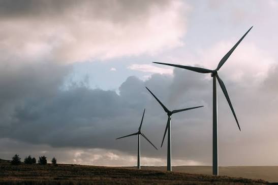 Tall white wind turbines standing on a green hillside against a cloudy sky
